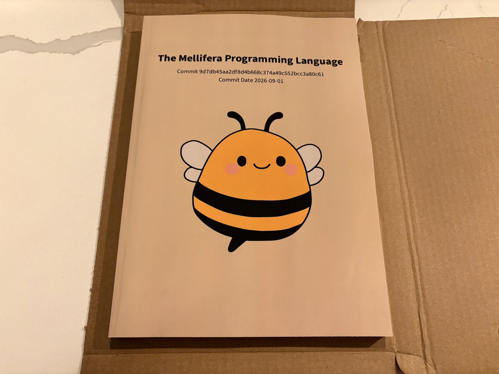The same cardboard package from before, now opened to review the Mellifera book, titled "The Mellifera Programming Language".